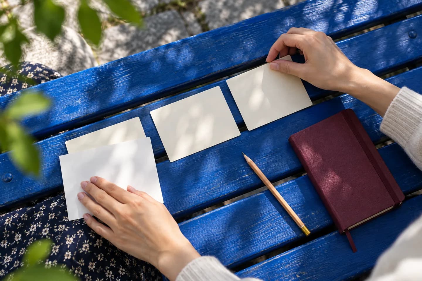 Hands arranging study cards on a blue bench beside a burgundy notebook