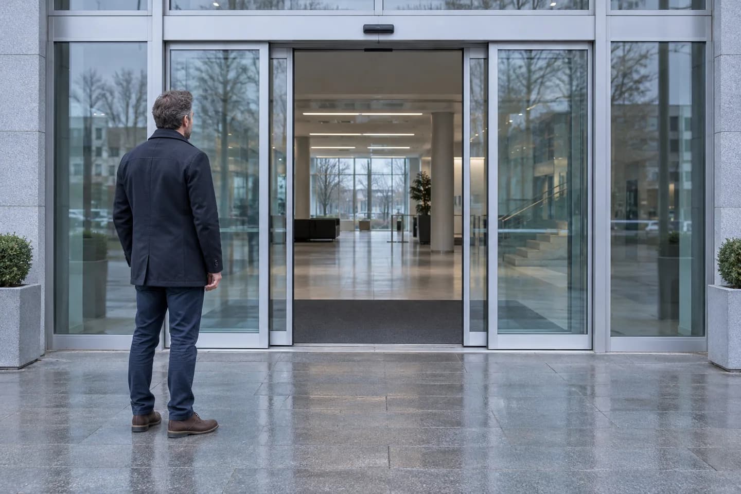 European man watching an open automatic glass entrance from a few steps away
