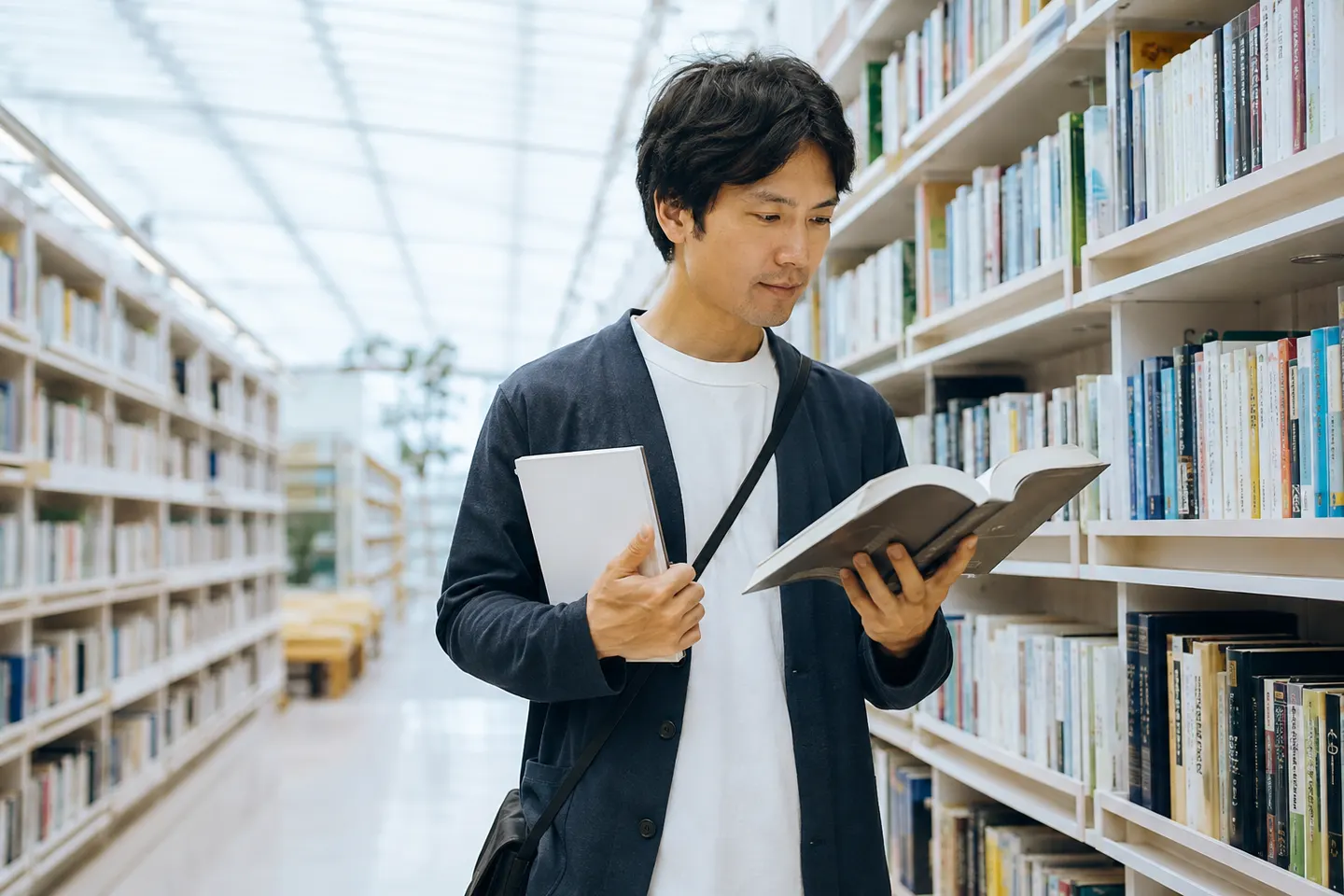 Pessoa adulta compara em uma biblioteca clara um caderno iniciante com um livro de leitura japonesa mais denso