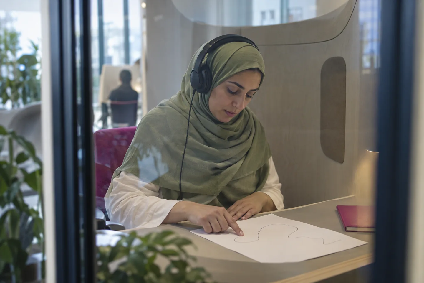 Adult learner following a simple pitch line while listening in a pale wooden sound-archive booth